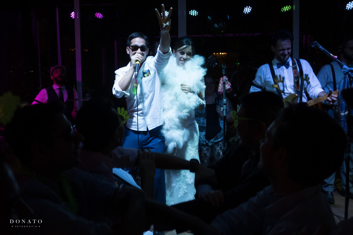 Noivo e noiva sobem no palco da banda Pertrini e cantam.