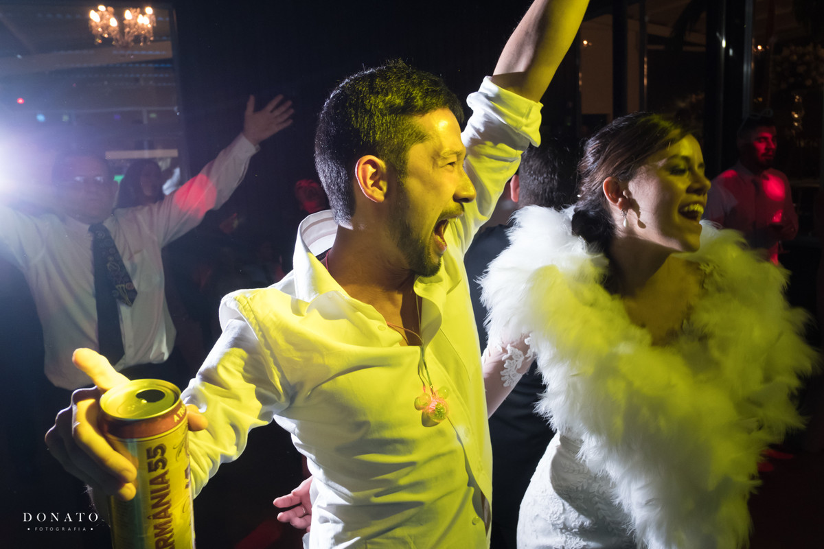 Noivo solta um grito de alegria, abraçado com a noiva no meio dos convidados da balada.