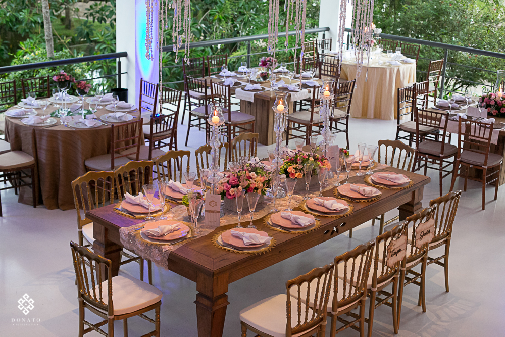 mesa compartilhada em madeira, com decoraçao em cor rosa, e guardanapos de pano brancos.