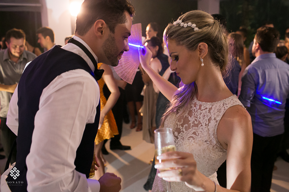 noivos sse divertem na pista de dança, a noiva esta tomando um drink bonito e o noivo se diverte junto.