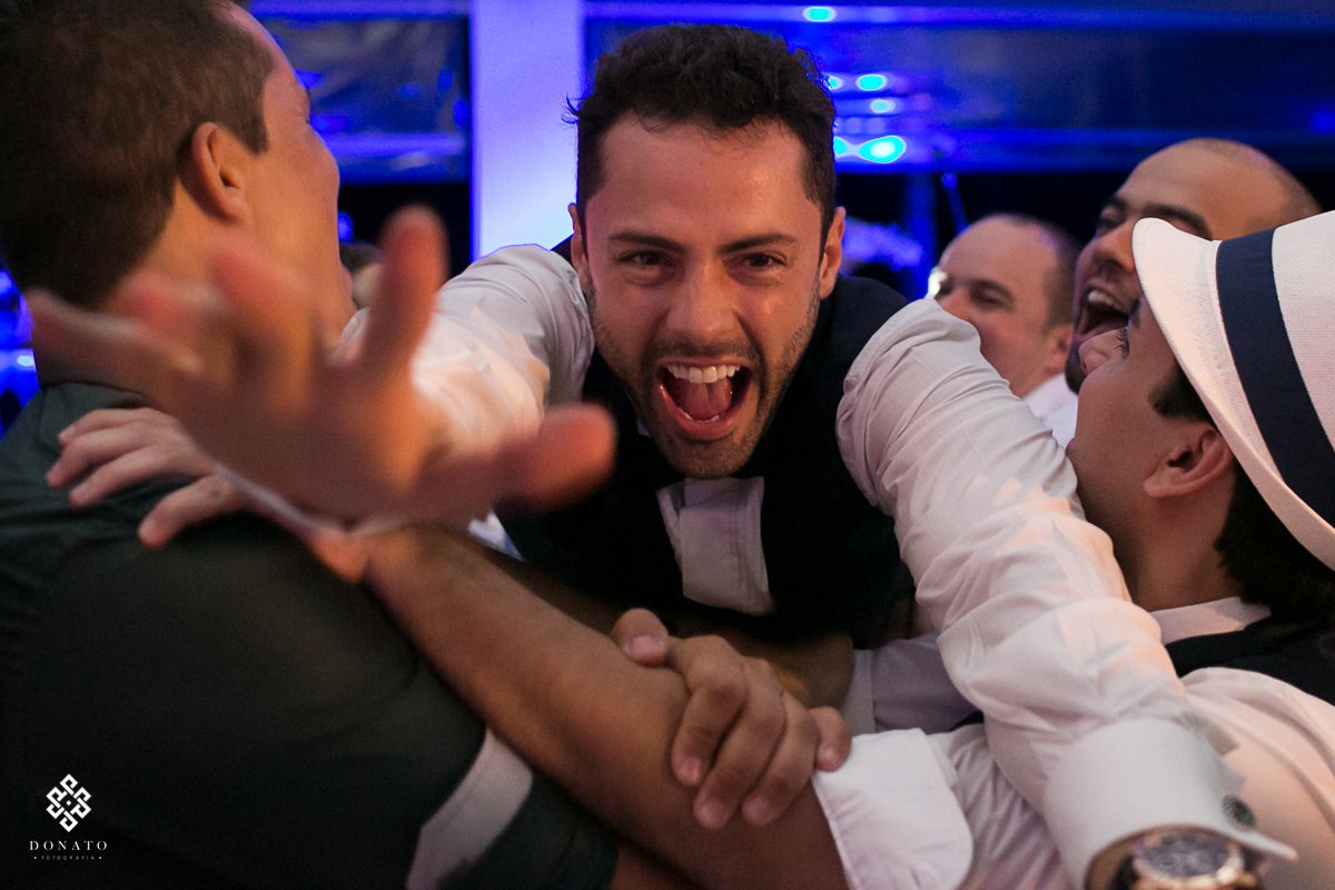 imagem do noivo caindo no braço dos amigos, olhando direto para camera com um lindo sorriso de alegria.