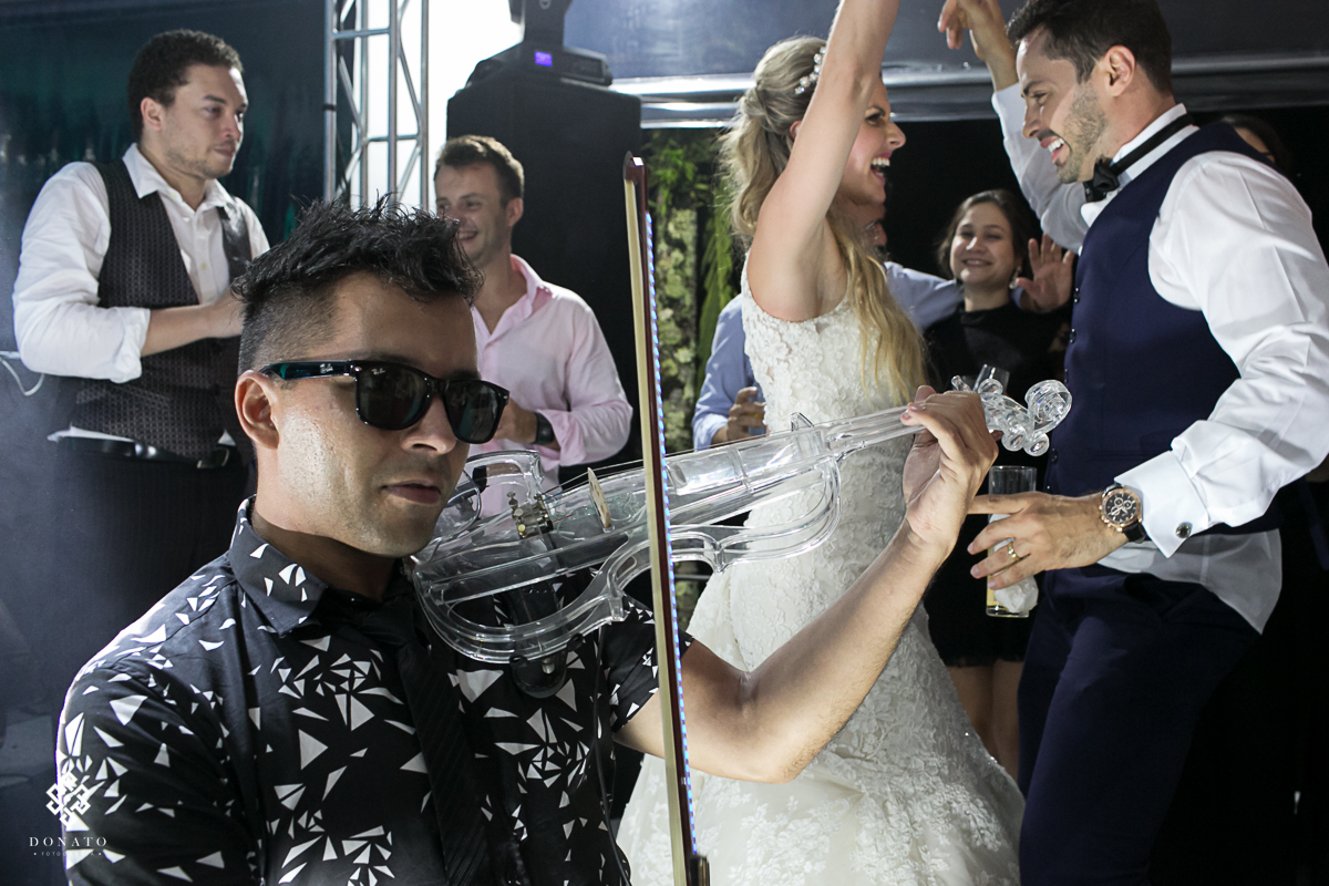 musico toca violino junto ao DJ, a noiva e noivo dançam ao fundo se divertindo muito.