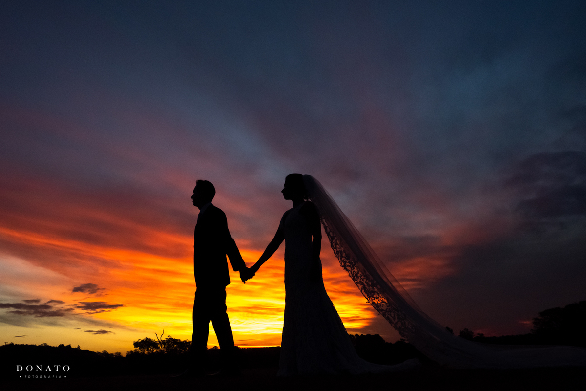 Noivos caminham com um lindo por do sol ao fundo.