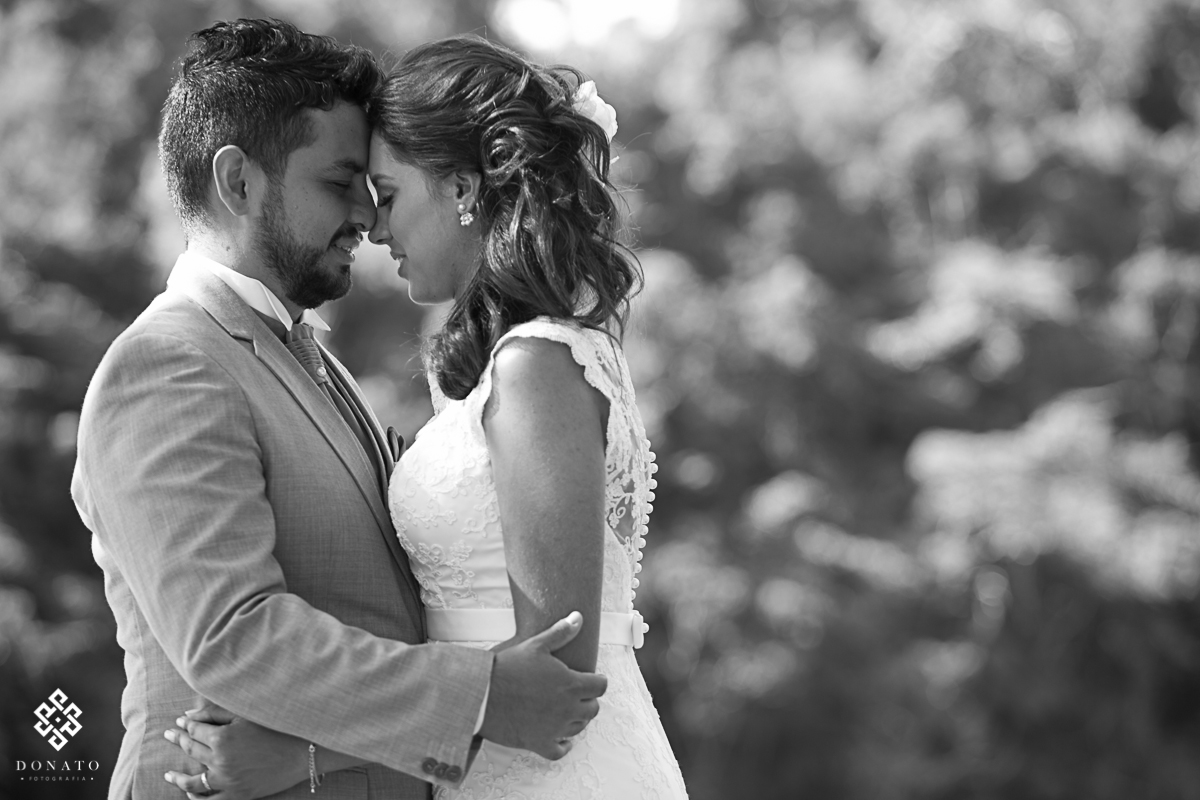 noivos encostam a cabeça e ao fundo temos arvores desfocadas.