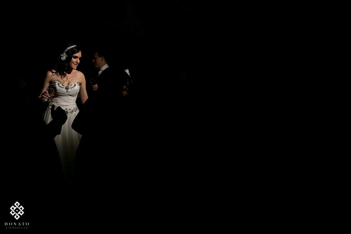 noiva em detalhe se divertindo no meio da pista, a luz utilizada deixa a noiva em evidencia entre uma grande parte escura.