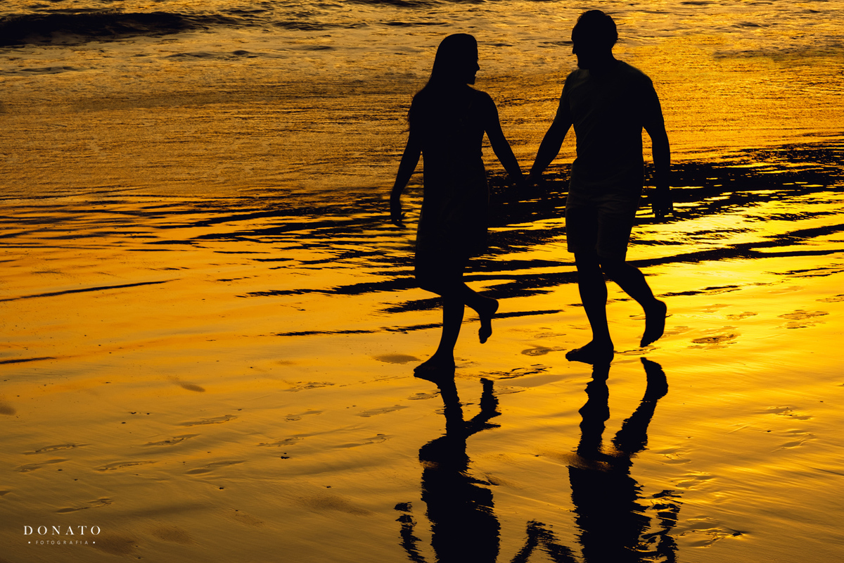Noivos caminhando a luz do por do sol na praia do Guarujá, esta fotografia é linda, com uma luz dourada maravilhosa.