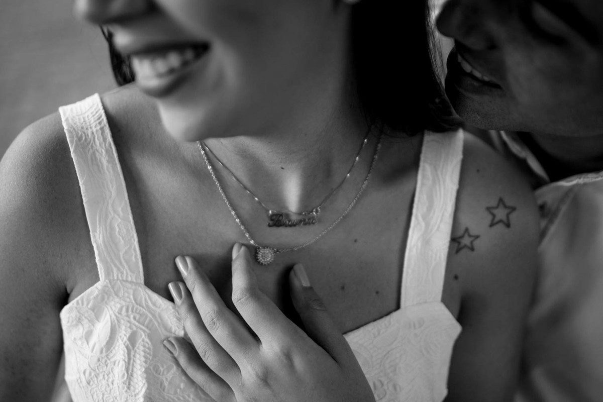 Foto do detalhe do colar da noiva, ela mexe com carinho e solta um sorriso lindo.