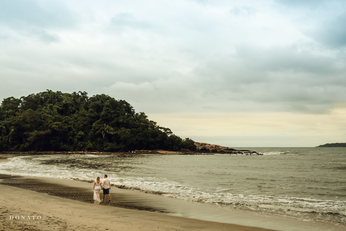 Noiva e noivo caminha na praia em dia nublado