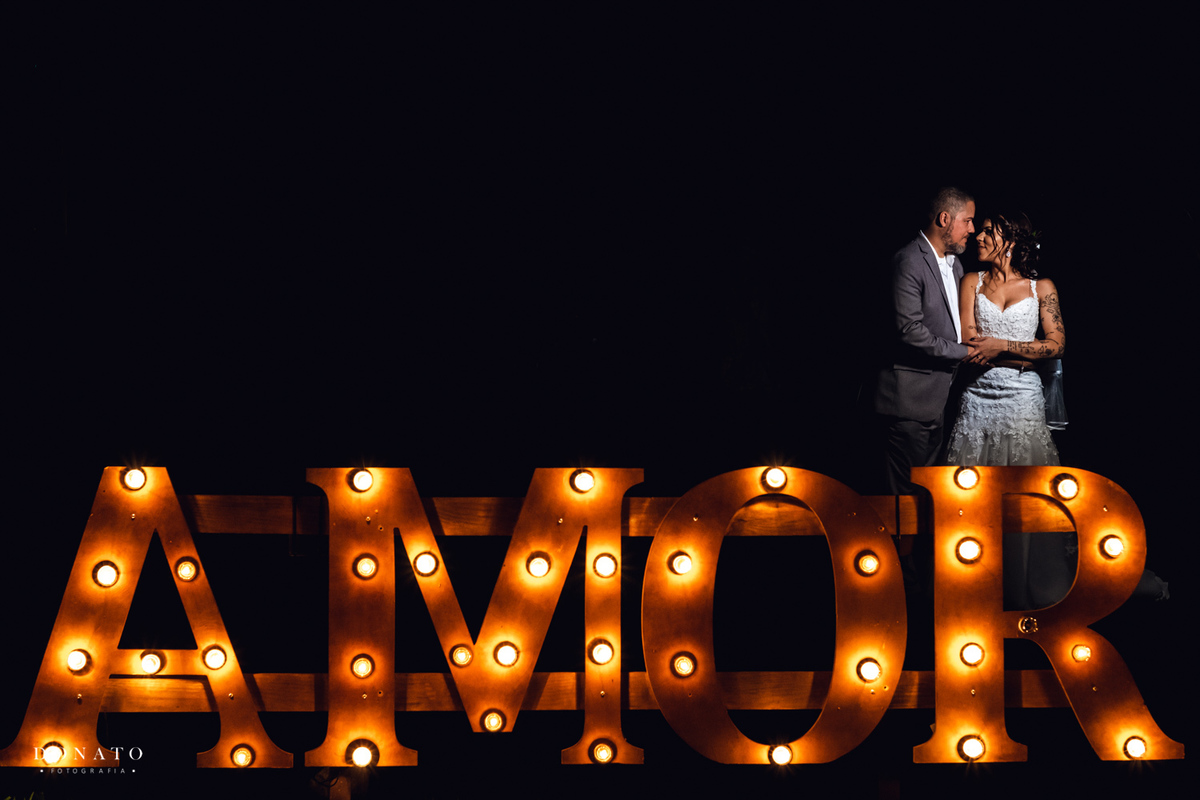 Retrato dos noivos em frente ao letreiro amor com luzinhas.