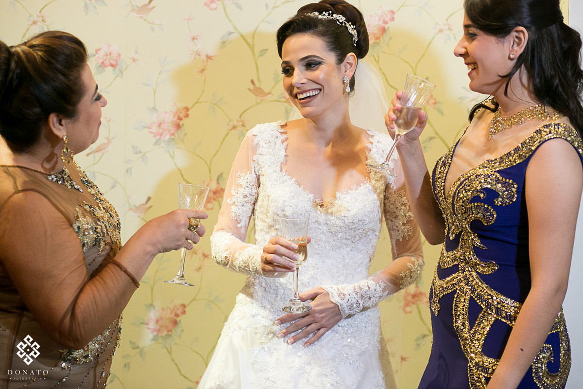 noiva já pronta brinda com irmã e mãe, tudo muito descontraído e alegre, com uma luz suave. Noiva usa vestido de renda feito por Pablo Stellai.