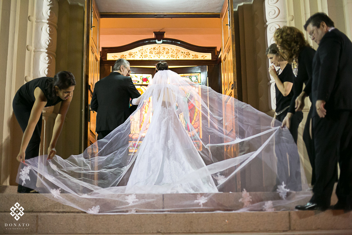 Noiva na porta da igreja, amigas arrumam o véu antes da entrada na igreja.