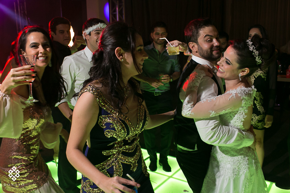 Noiva abraça o noivo e dança, com sua irmã ao lado se divertindo pra valer.