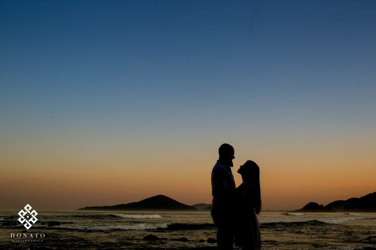 casal se abraça, imagem foi feita em silhueta, com os noivos escuros, com um fundo azul e marelo do por do sol.