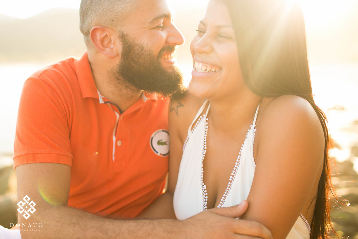 Imagem linda e impactante, onde os noivos soltam um sorriso muito alegre, o noivo com sua barba estilo lenhador, sendo contornada por uma luz dourada do sol, imagem transmite alegria.