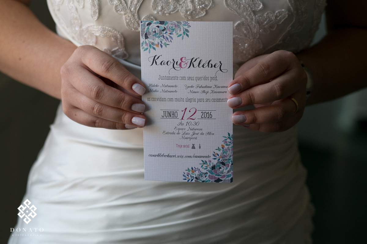 Noiva segura na mao o convite do casamento, a foto é do detalhe da mao com o convite.