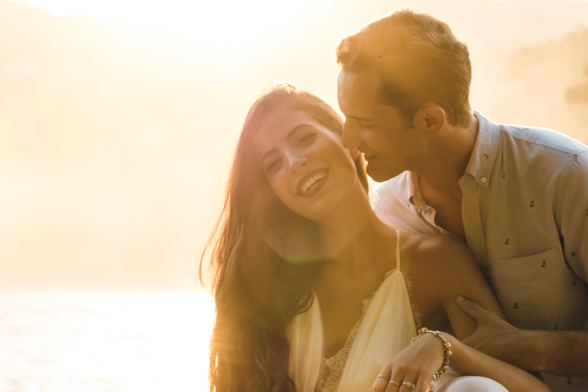 casal juntos da beijinho na praia com por do sol.