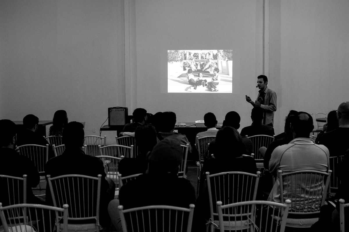 Donato palestra na frente de mais de 100 alunos, na tela ele mostra uma parte do seu curso de fotografia.