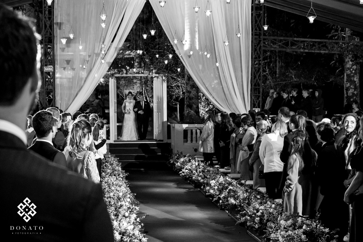 noiva entra toda de branco pelo corredor com flores brancas na fazenda 7 lagoas.