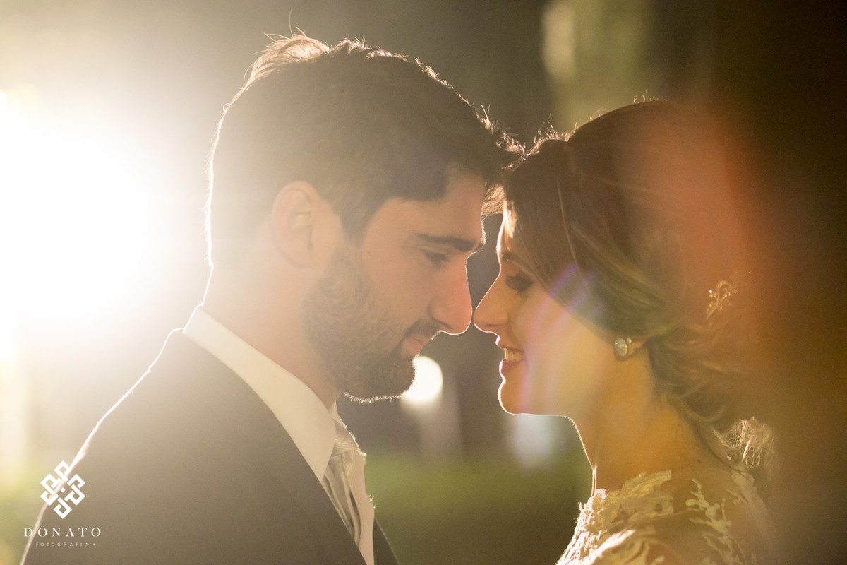 Noivos encostam o rosto enquanto uma luz linda entra e faz efeito amarelado.