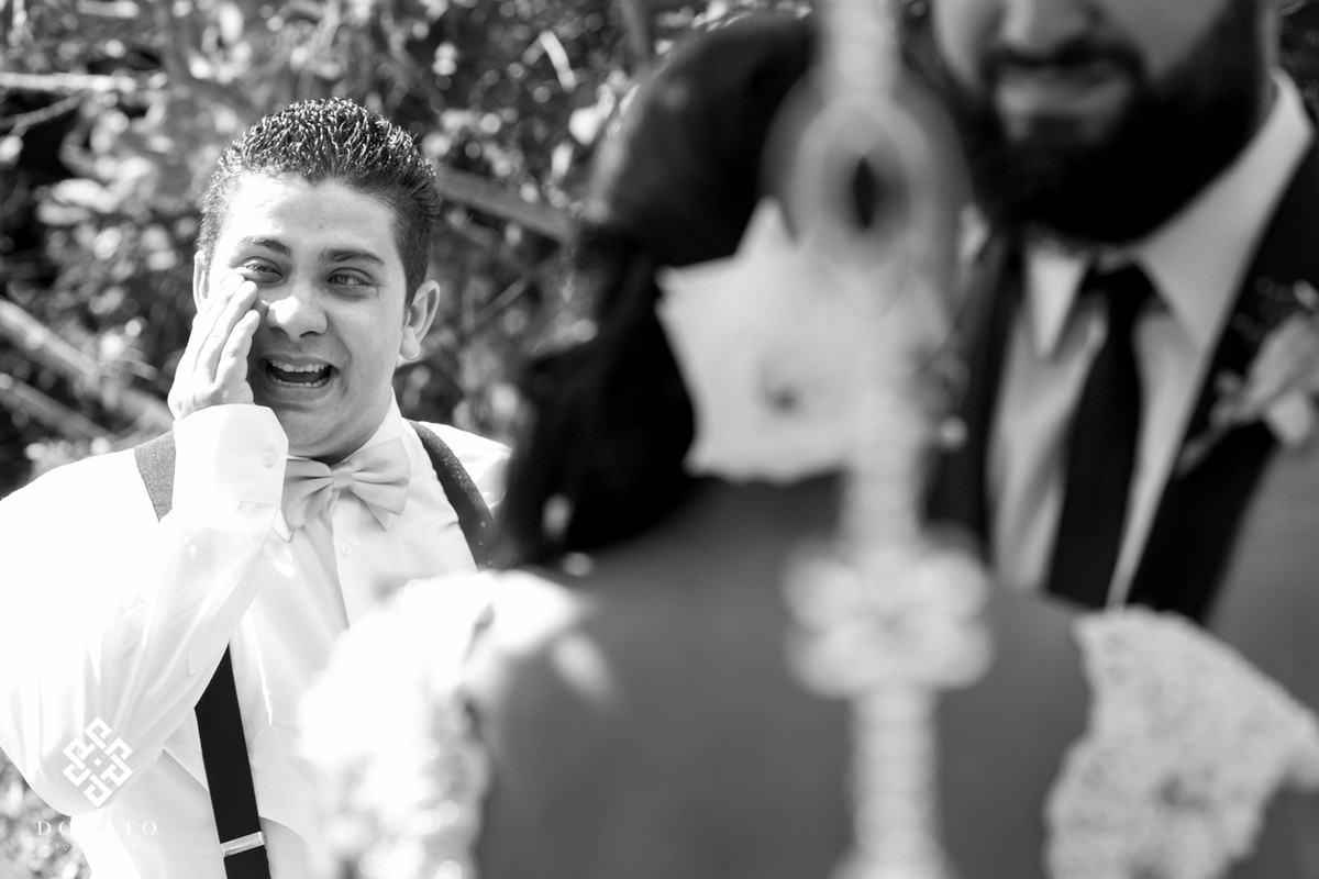 Padrinho chora ao fundo e limpa a lagrima, enquanto os noivos trocam os votos.