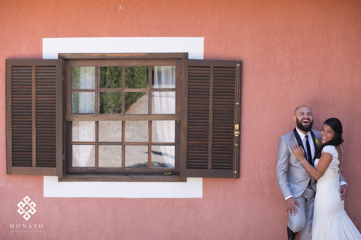 Noivos namoram em frente a janela do espaço natureza, a parede de cor salmão da um efeito legal a foto.