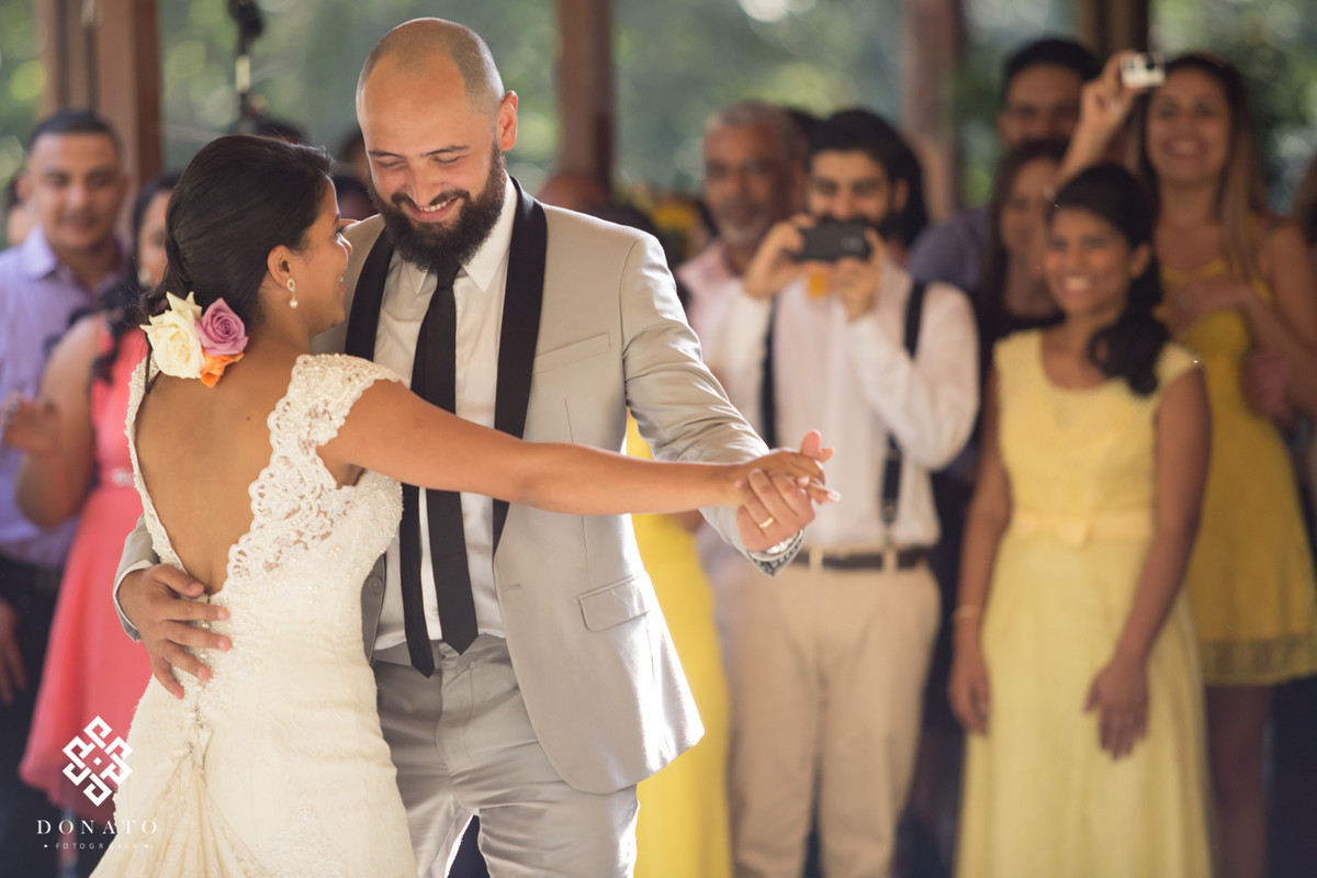 Noivos dançam a valsa com os padrinhos ao fundo.