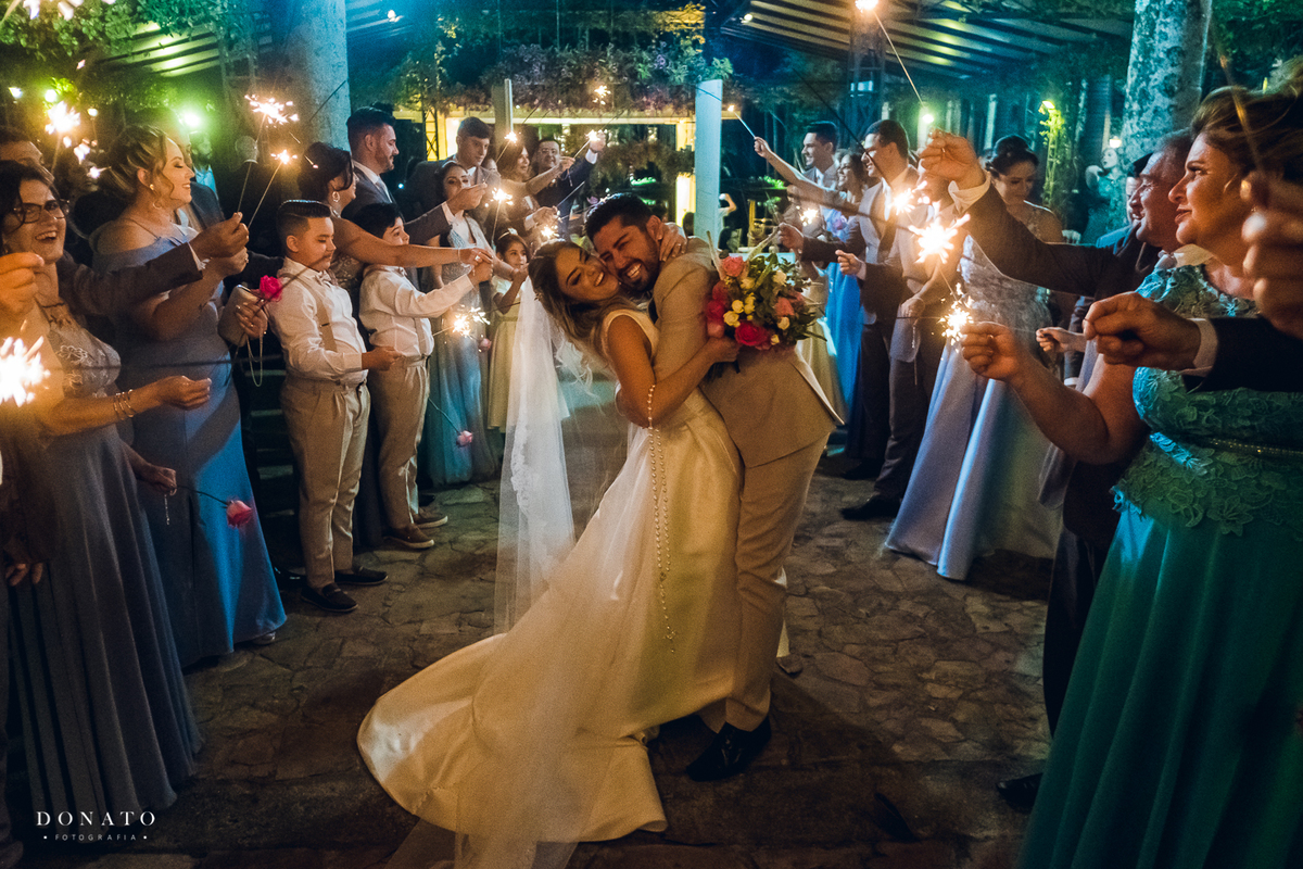 Noivos se abraçam entre os sparkos , bastão de luz na saida dos noivos.