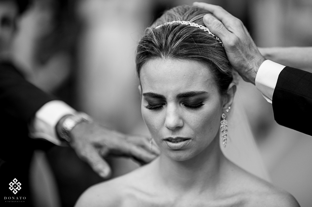 mae e pai colocam a mão na cabeça da noiva, dando sua bençao.