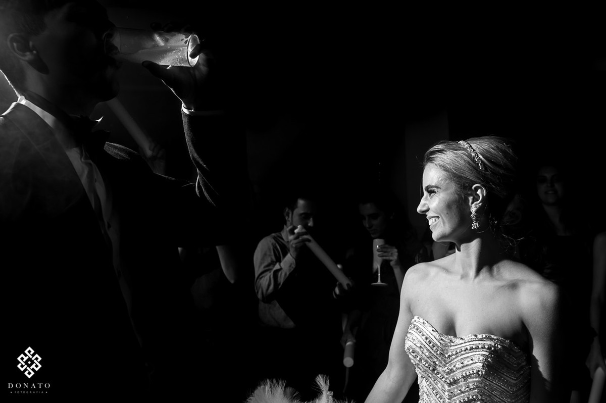 noivo toma um copo de cerveja e a noiva se diverte ao fundo.