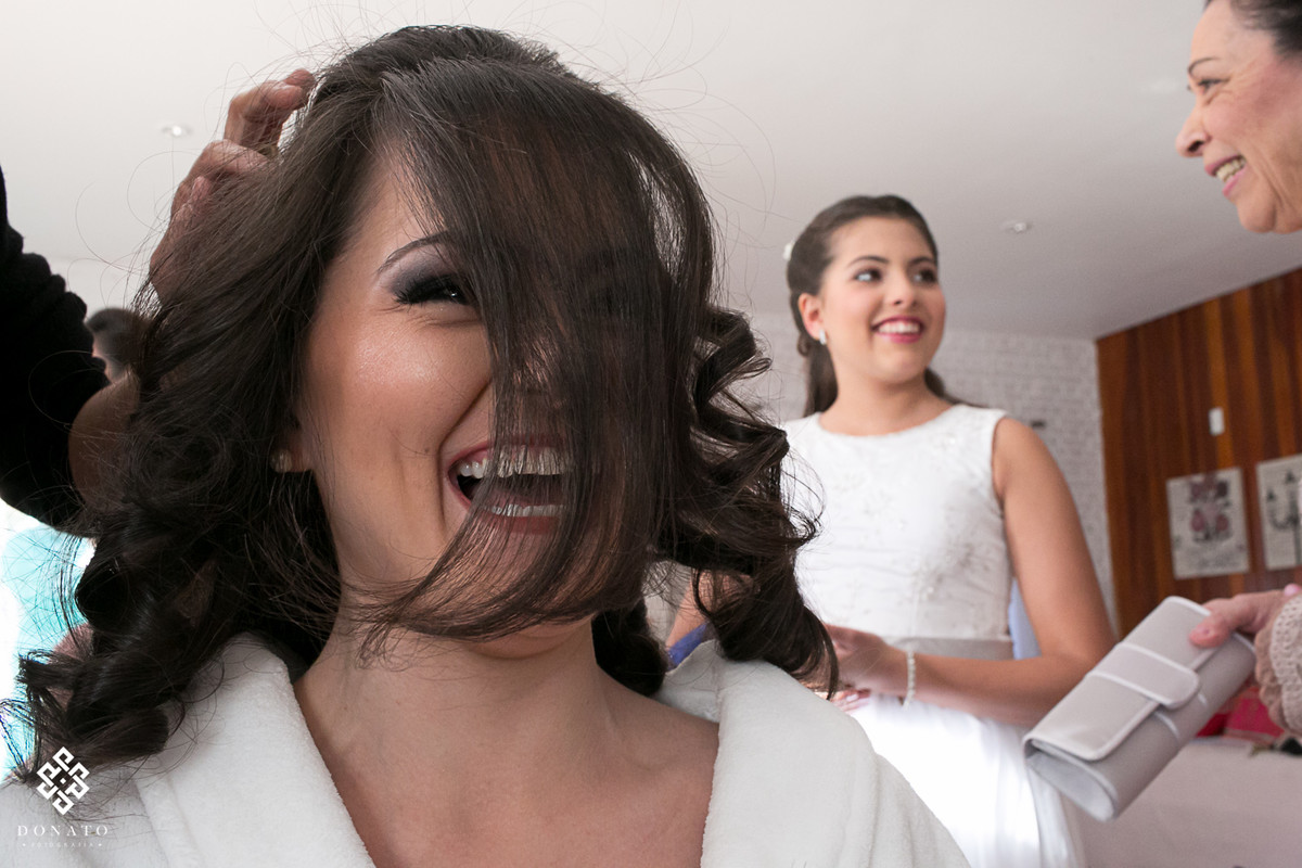 noiva se diverte enquanto seu cabelo esta sendo arrumado, a linda franja e seu sorriso deixam a imagem linda.