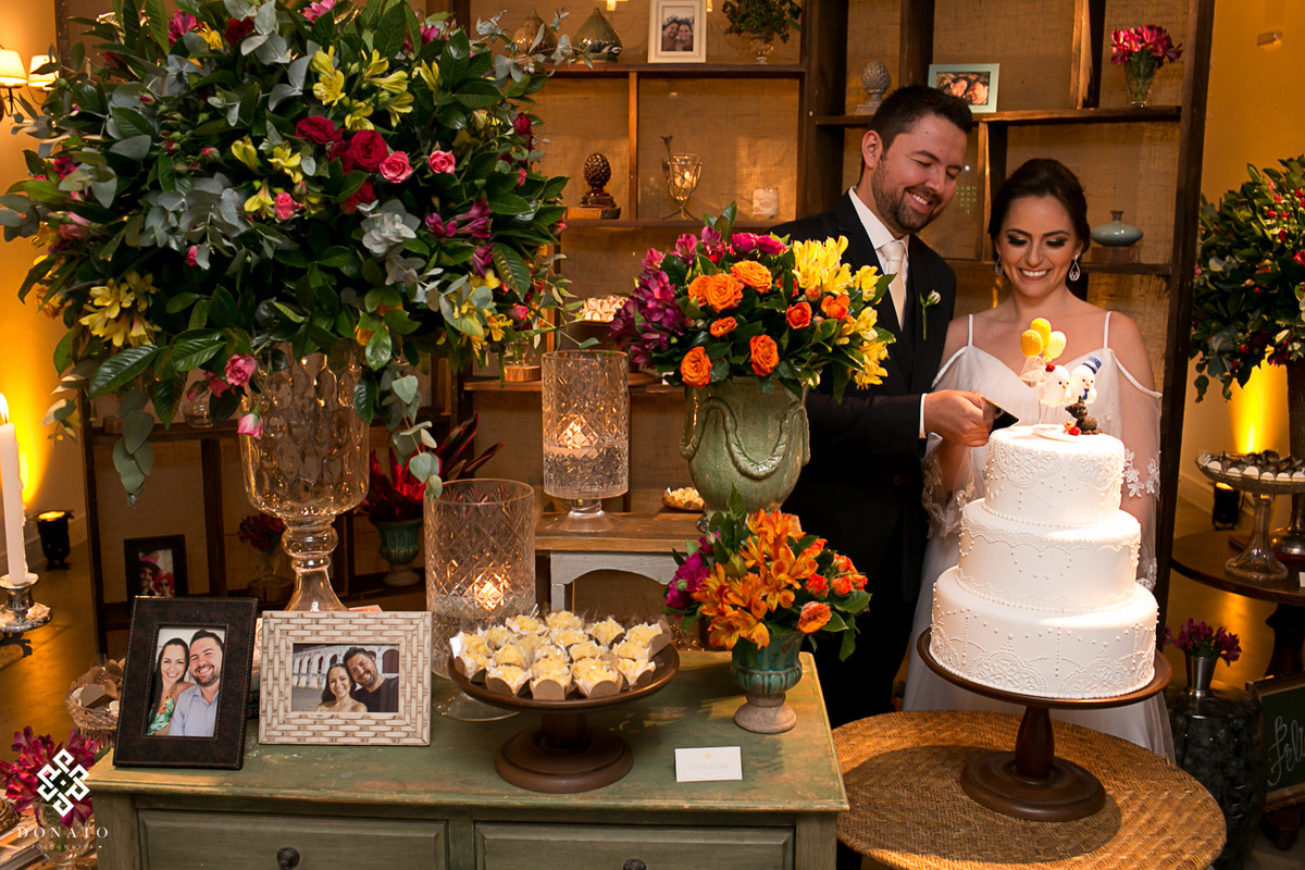 noivos brindam em frente a mesa de bolos e a linda estante de detalhes.