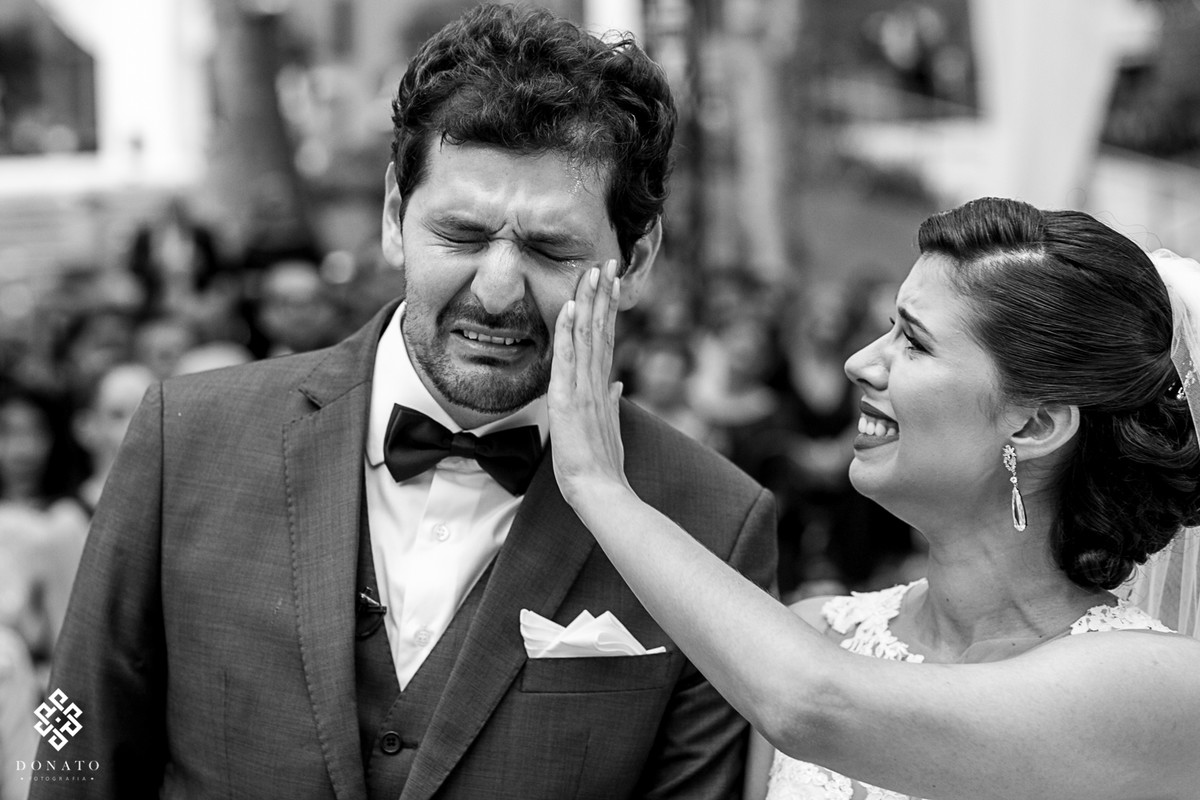 Foto emocionante, com a noiva secando as lagrimas do rosto do noivo.
