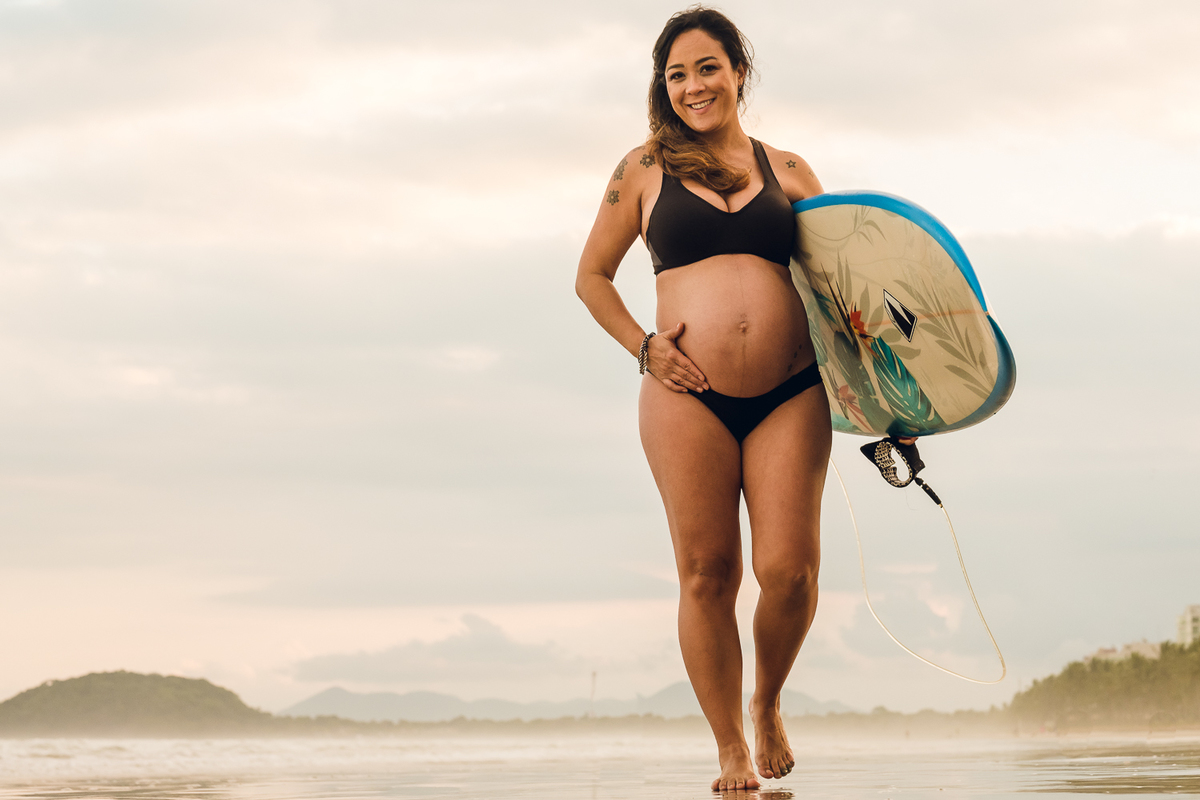 Gestante com prancha de surf no por do sol