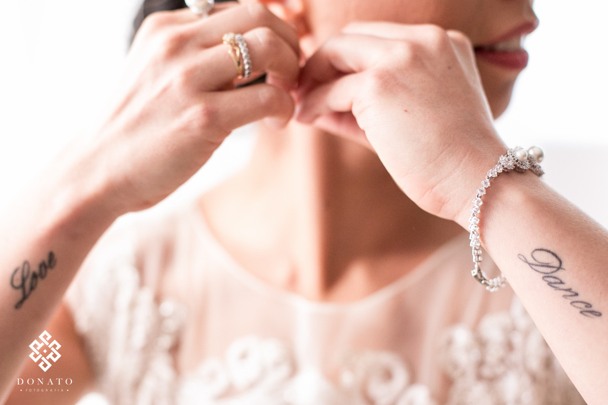 A noiva coloca os brincos, nesta foto da pra ver duas tatuagem que tem tudo haver com a noiva que é bailarina, onde esta escrito love e dance.
