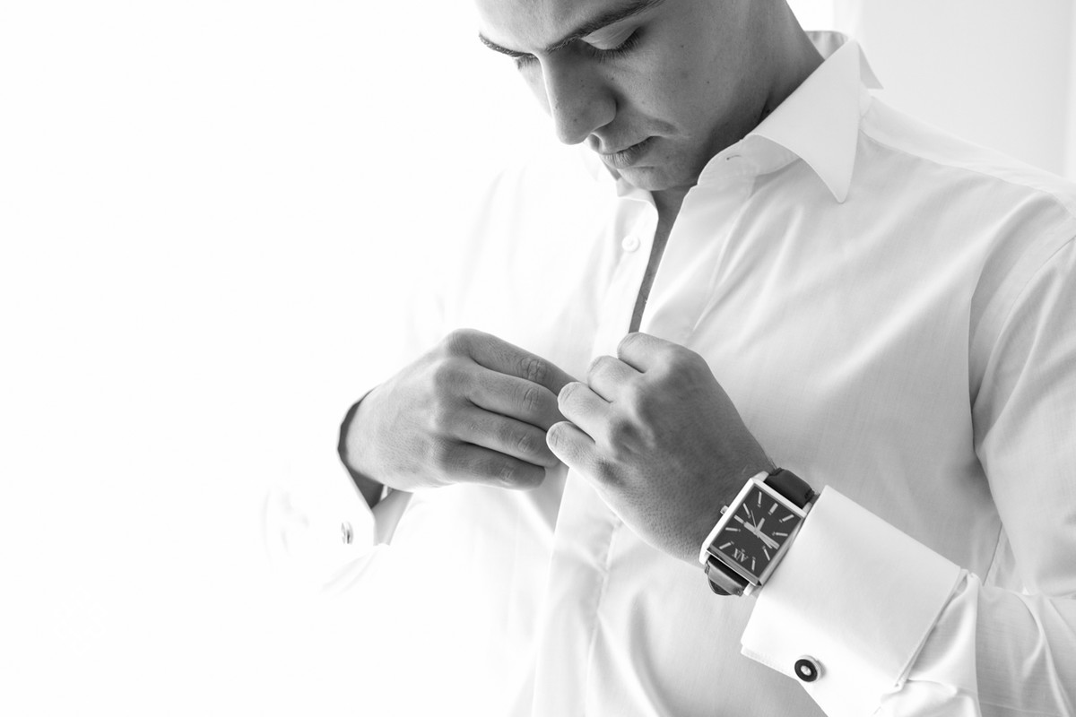 Noivo se prepara para o casamento, arrumando a camisa no seu making of.