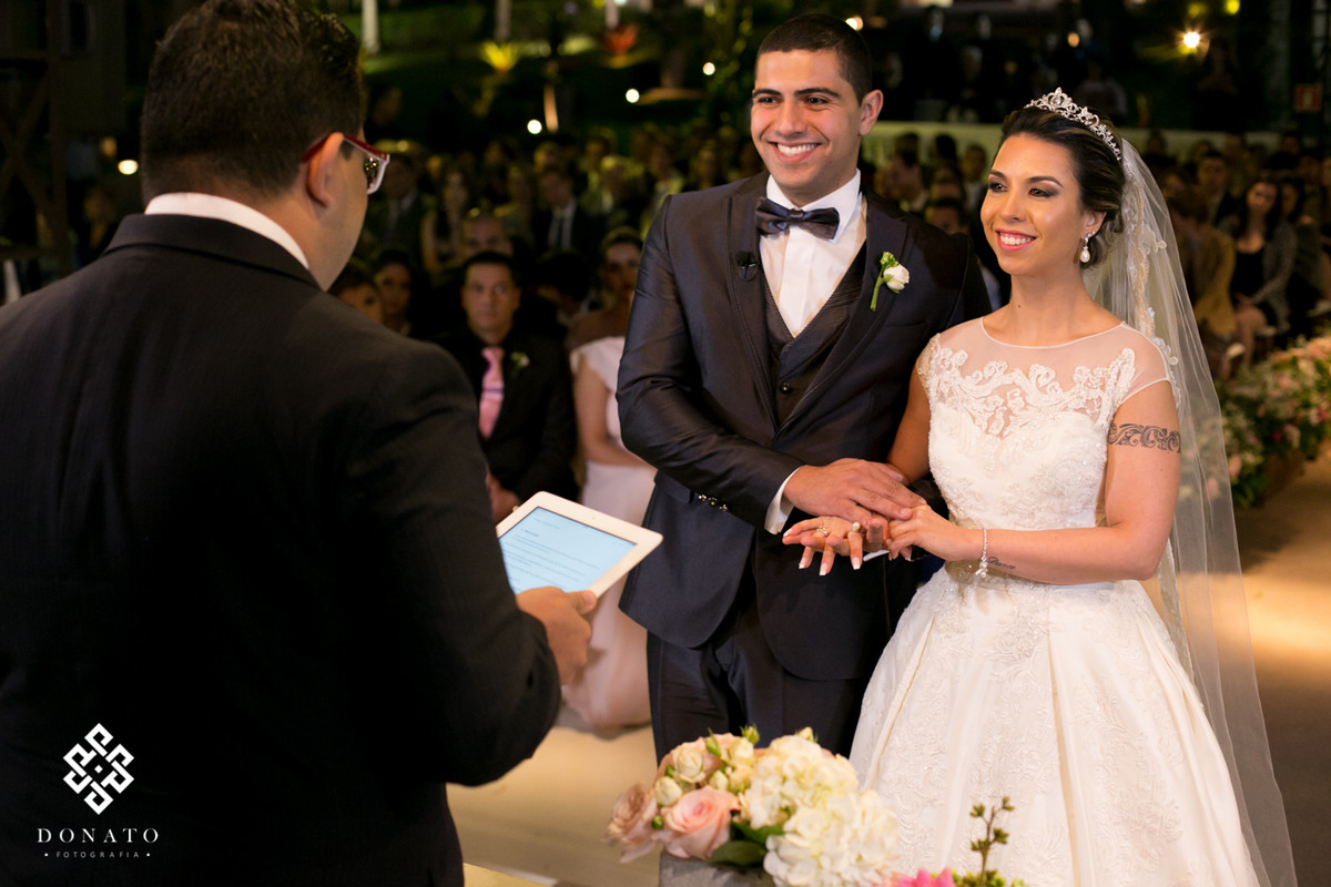 Noivos prestam atençao e sorriem na cerimônia.