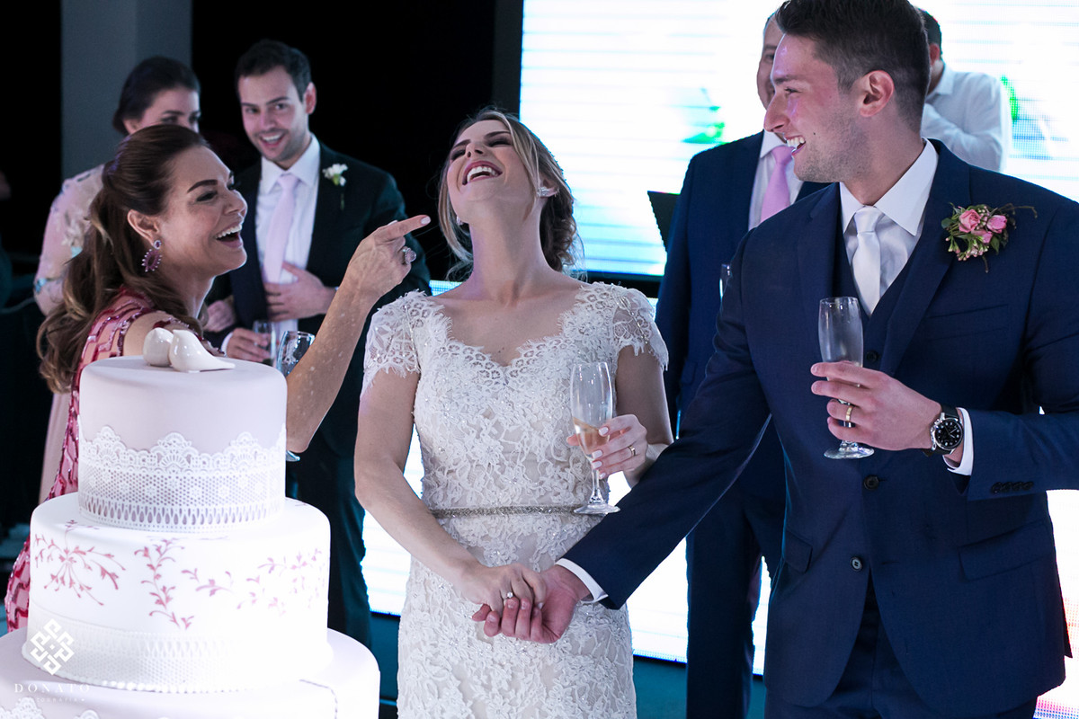 Noivos cortam o bolo e a mão aponta o dedo dando um recado divertido.