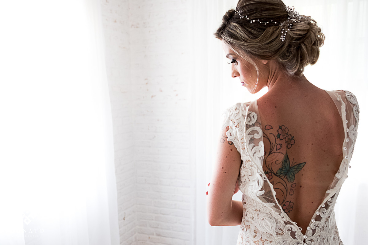 Noiva deixa a mostra a tatuagem nas costas ao fechar o vestido Lucas Anderi.