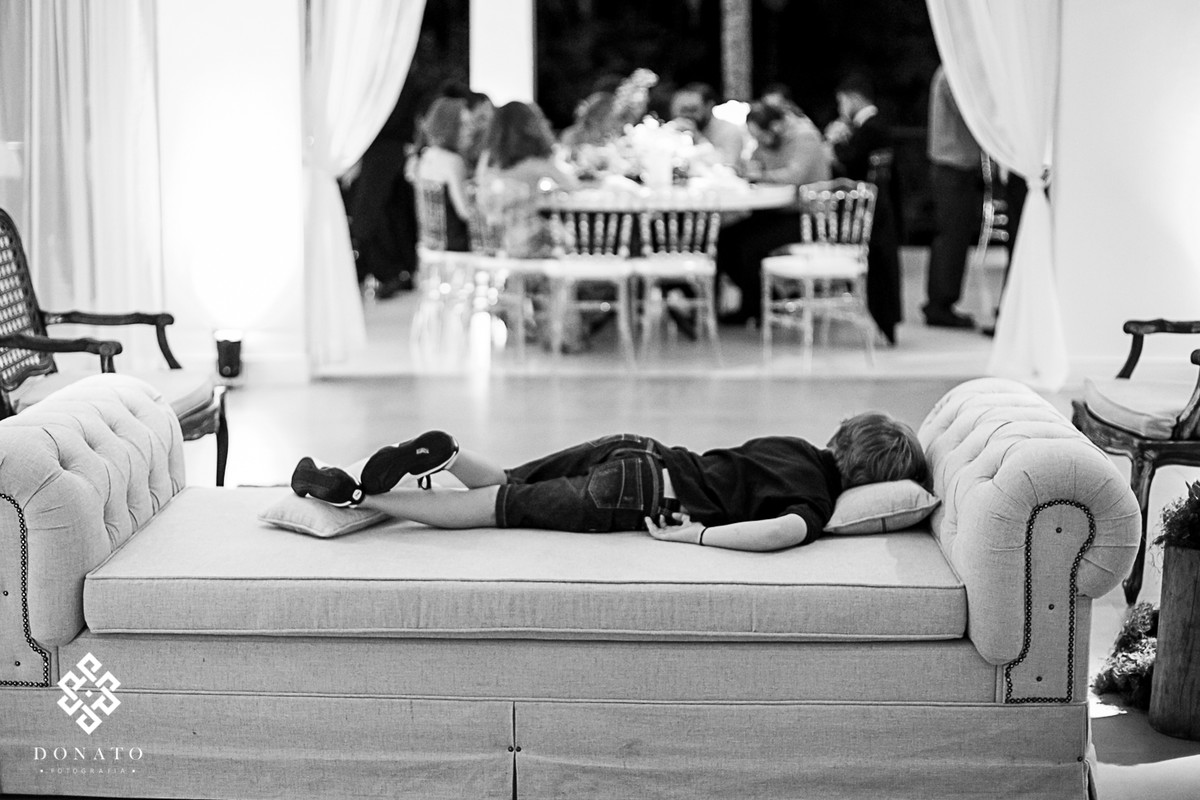 Menino dorme no sofá da fazenda enquanto a festa continua.