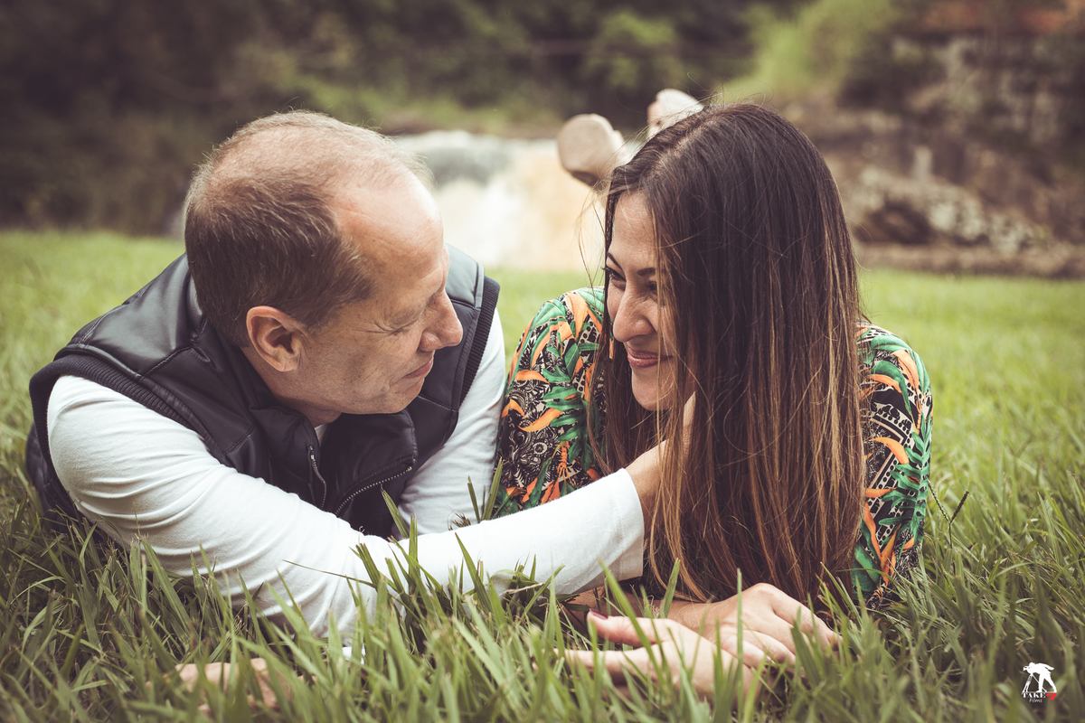 carinho de casal de noivos deitados na grama com cachoeira de fundo 