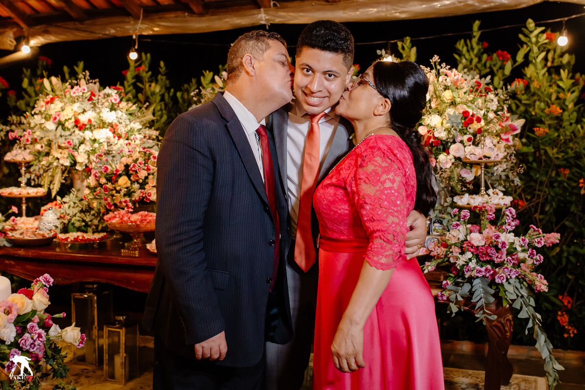 Pais do noivo beijando o noivo na  mesa do bolo