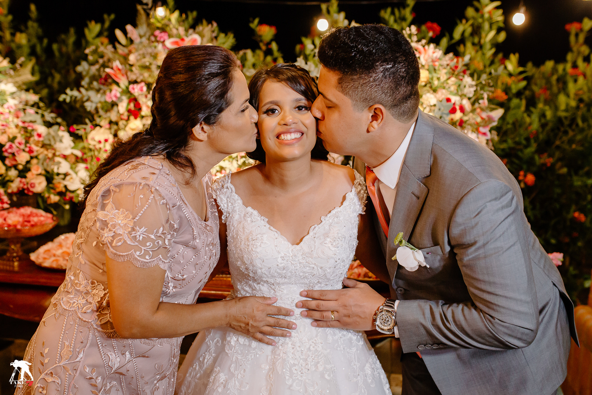 mãe da noiva com o noivo beijando a noiva na mesa do bolo 