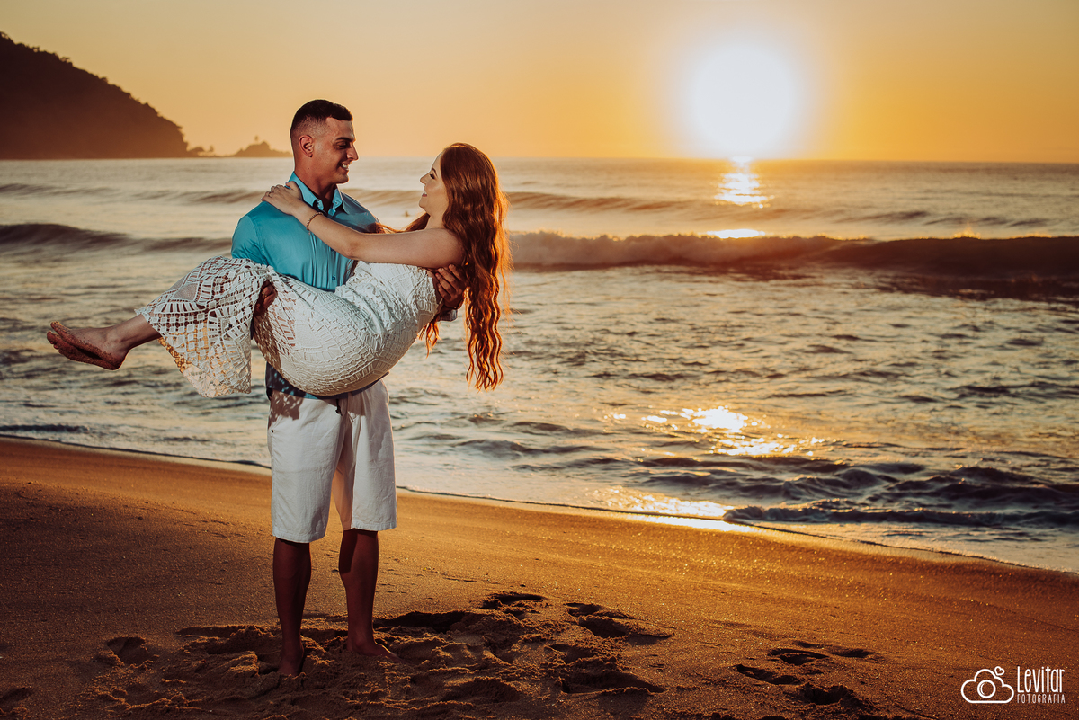 noivo com sua noiva no colo e ao fundo sol refletindo no mar