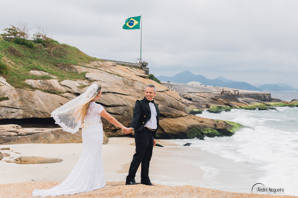 de mãos dadas os noivos caminham pela areias do forte de copacabana clicados pelo fotografo de casamento rj andre nogueirafotografia durante o ensaio trash the dress fotografia de casamento rj