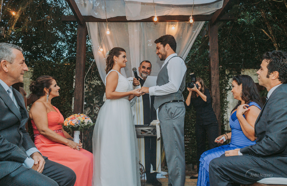 a noiva coloca a aliança no dedo do noivo e observado pelos pais