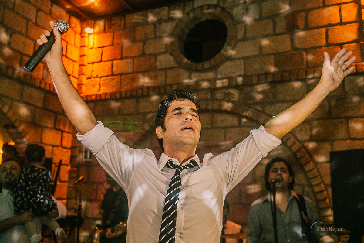 pai do noivo com os braços esticados e segurando o microfone