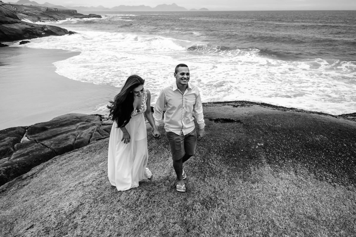 casal sindo a pedra do forte de copacabana de mãos dadas e sorrindo
