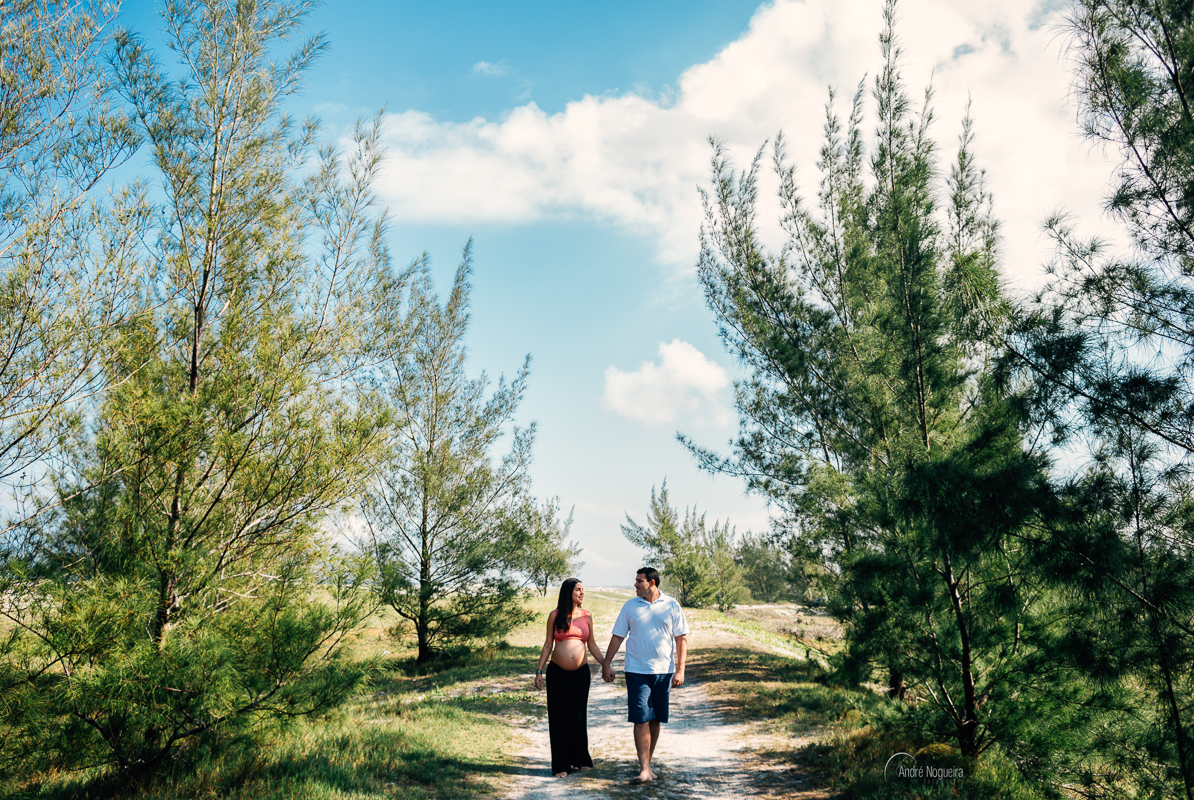 linda gestante e seu marido caminhando entre dois pinheiros de mãos dadas, na praia grande em cabo frio