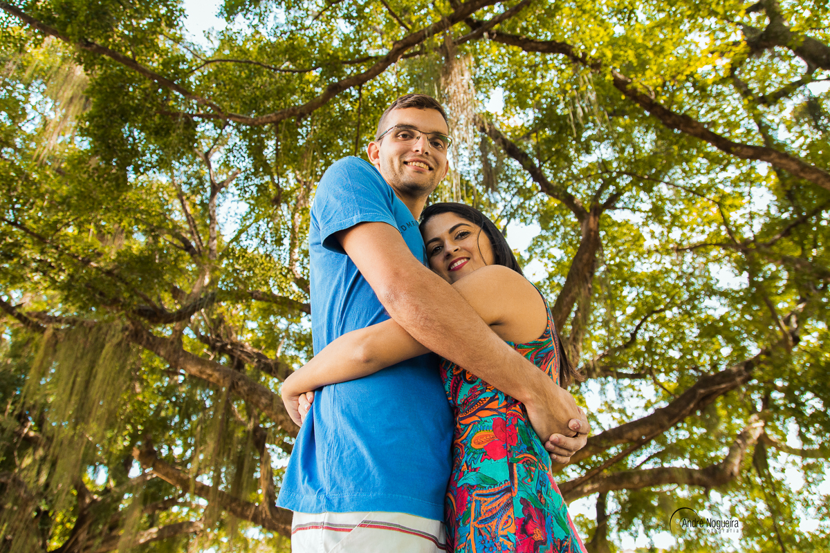 em baixo de uma grande árvore linda, tem um casal apaixonado abraçado.