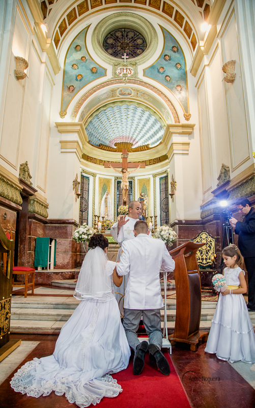 os noivos ajoelhados no altar sendo abençoado pelo padre